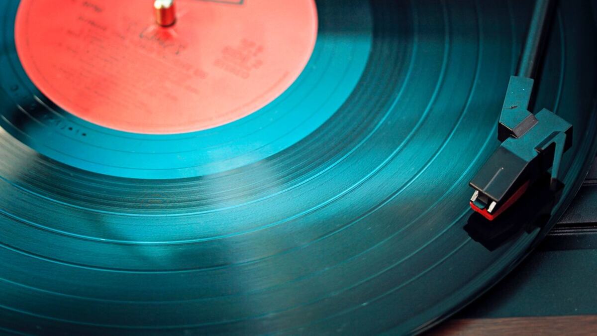 A tonearm resting on a spinning teal vinyl record