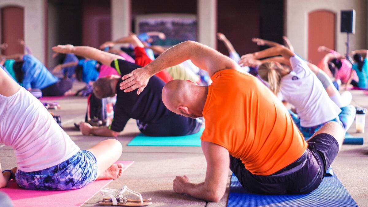 A large outdoor yoga class mid side-stretch on colourful mats